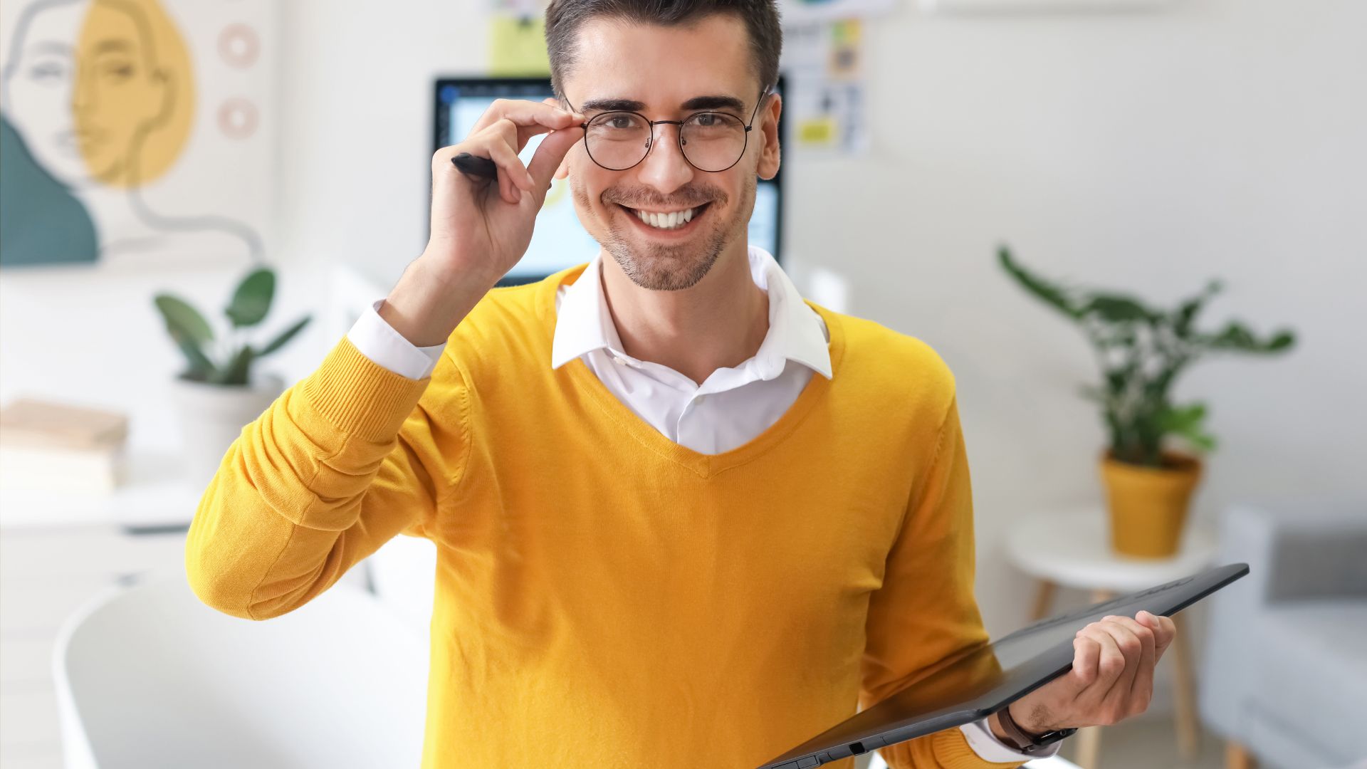 A graphic artist wearing glasses is holding a tablet in his hands.