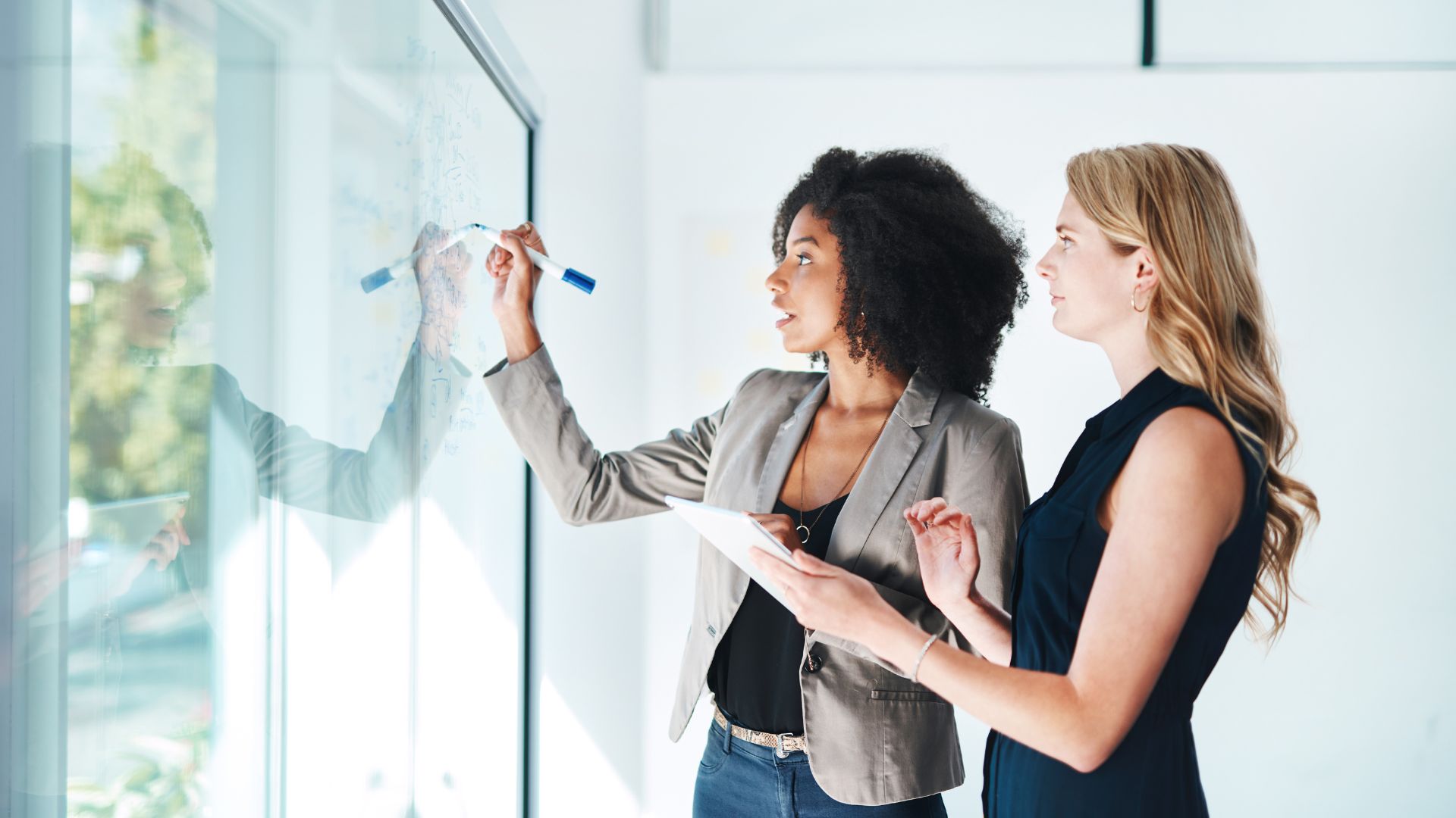 Two business women standing in front of a glass wall.