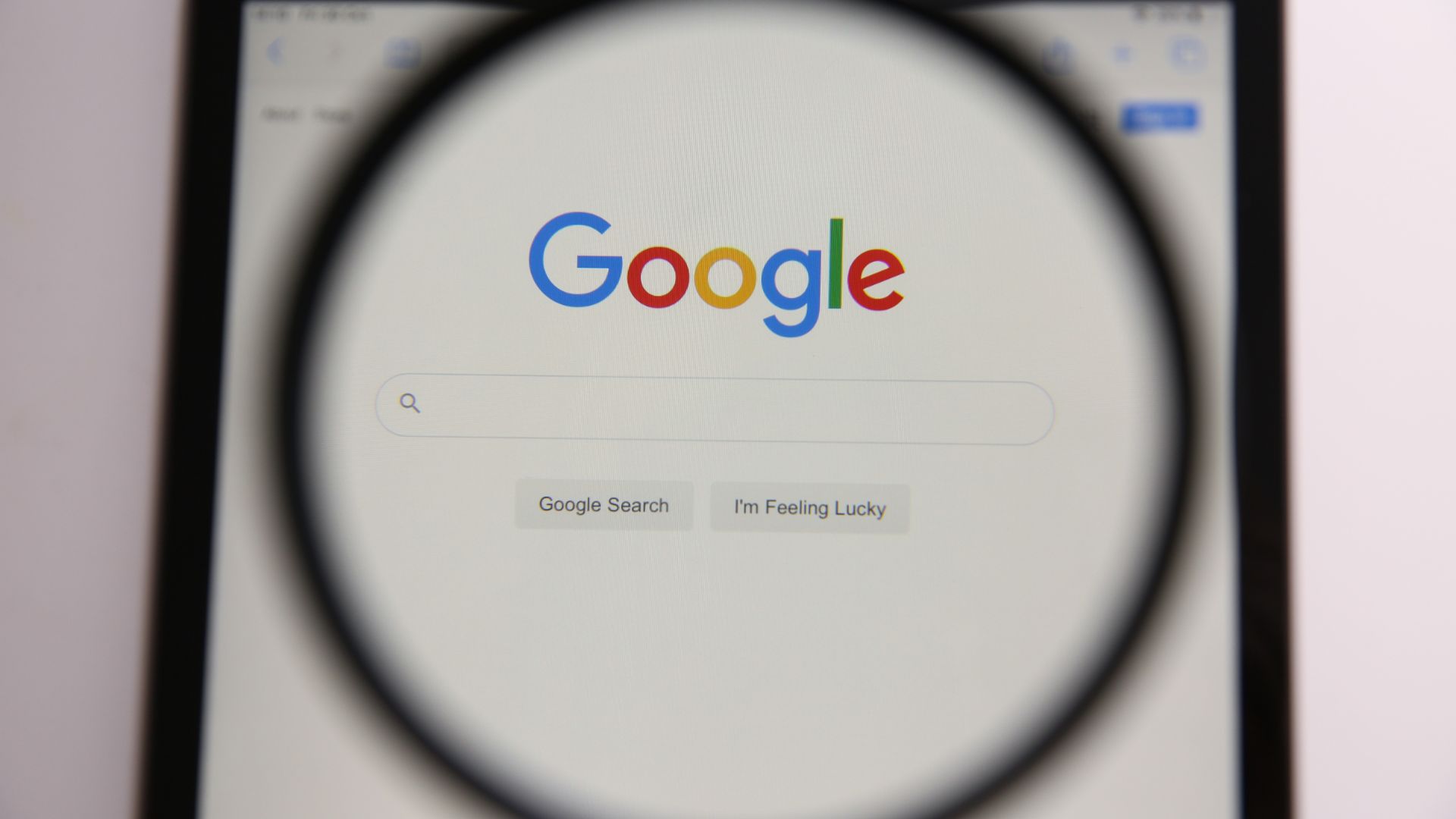 The google logo is seen through a magnifying glass on a smartphone.